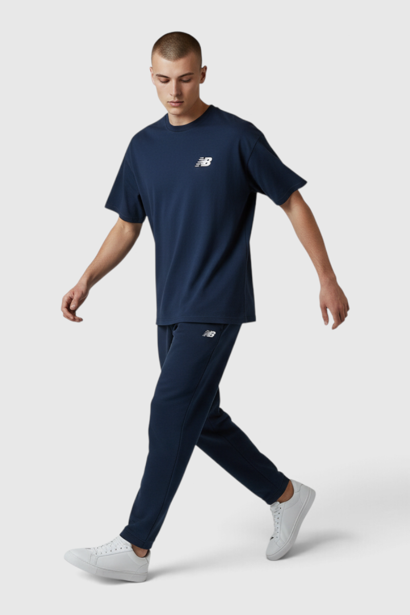 Sporline New Balance lacivert %100 pamuk erkek tişört giyen model, gri arka plan üzerinde yürürken.